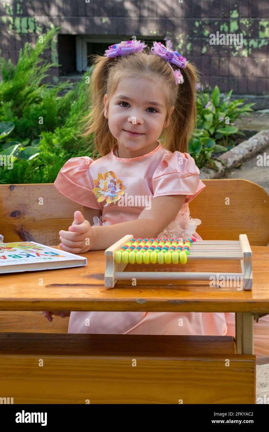 Little beautiful schoolgirl sits at a desk with books on the background ...