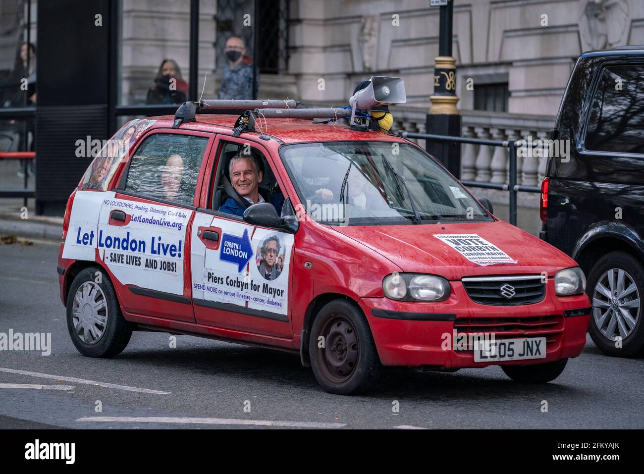 London, UK. 4th May 2021. Piers Corbyn ‘battle bus’ continues its rounds of Westminster. Campaigner Heiko Khoo drives in circles around central London with posters displaying’ Vote Corbyn’ and ‘Let London Live’ covering the sides of a rickety red car with a megaphone strapped to the top. Piers Corbyn, a London mayoral candidate, plans to end ‘Covid con rules’ and reverse discriminatory treatment against those who refuse to wear a mask. Credit: Guy Corbishley/Alamy Live News Stock Photo