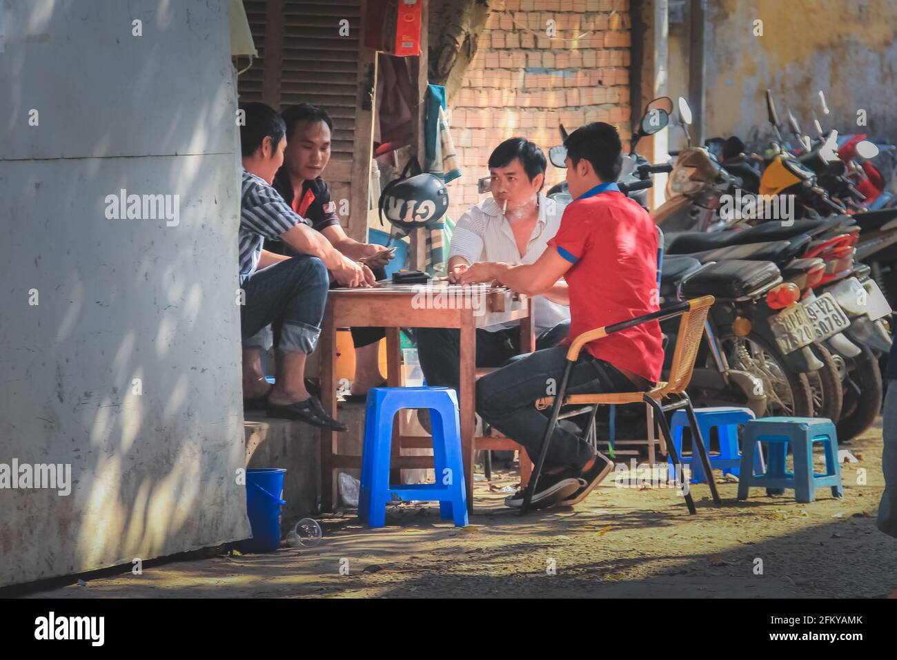 Ho Chi Minh City, Vietnam - March 10 2014: Local Vietnamese men gambling playing street poker card game on a discreet, urban backstreet alley in Saigo Stock Photo