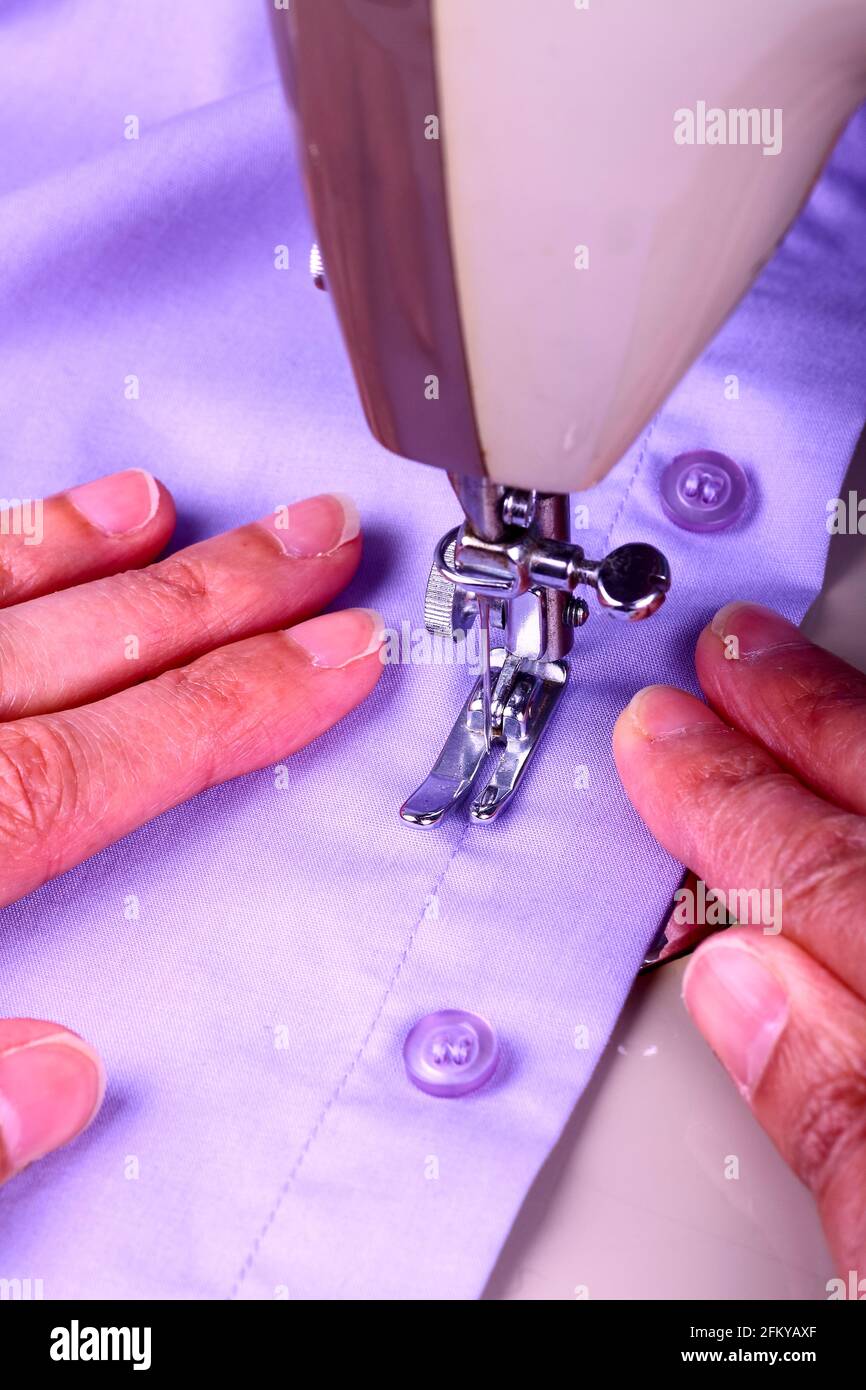 Close up of a vintage sewing machine and ladies hands guiding a cotton shirt that's being stitched Stock Photo