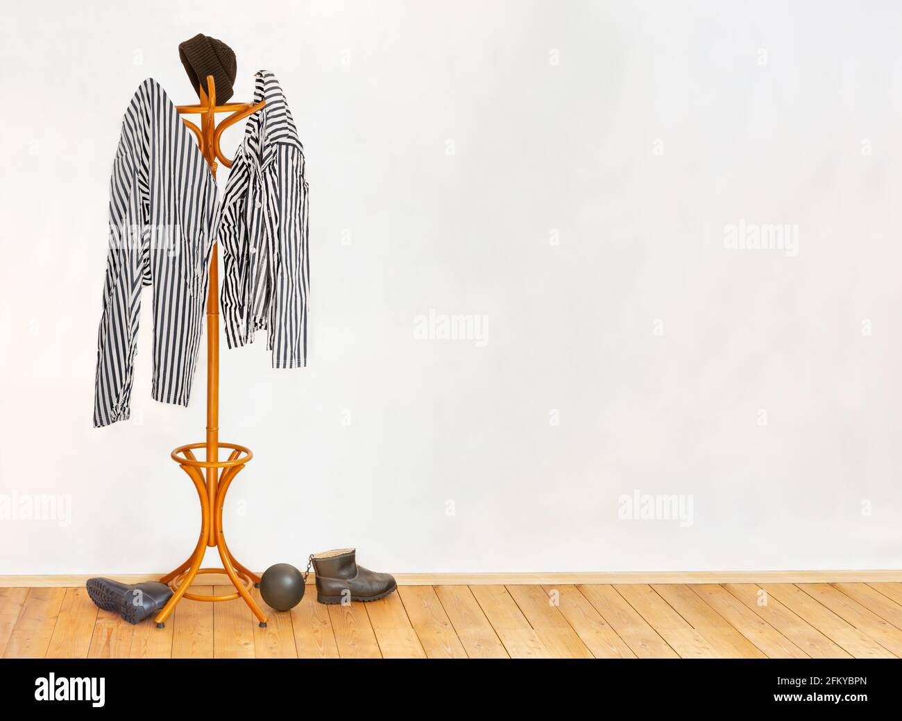 The striped prisoners costume hangs on the coat hook in an empty cell with wooden floor. Stock Photo