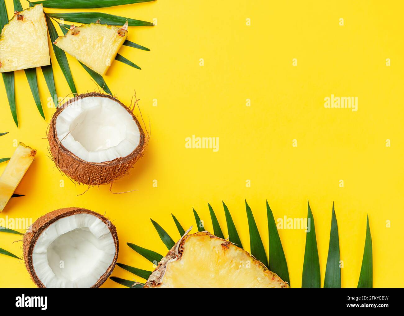 Broken coconut and pineapple slices on bright yellow background. Flat lay, copy space. Stock Photo
