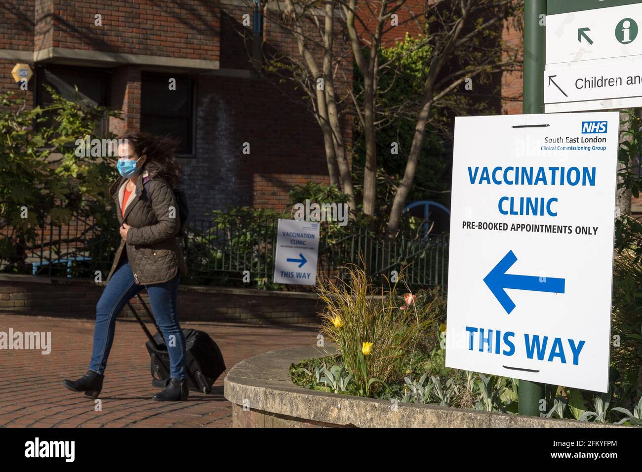 woman in face mask carries a suitcase out of Vaccination Clinic at Bromley Civic Centre, Kent, England Stock Photo