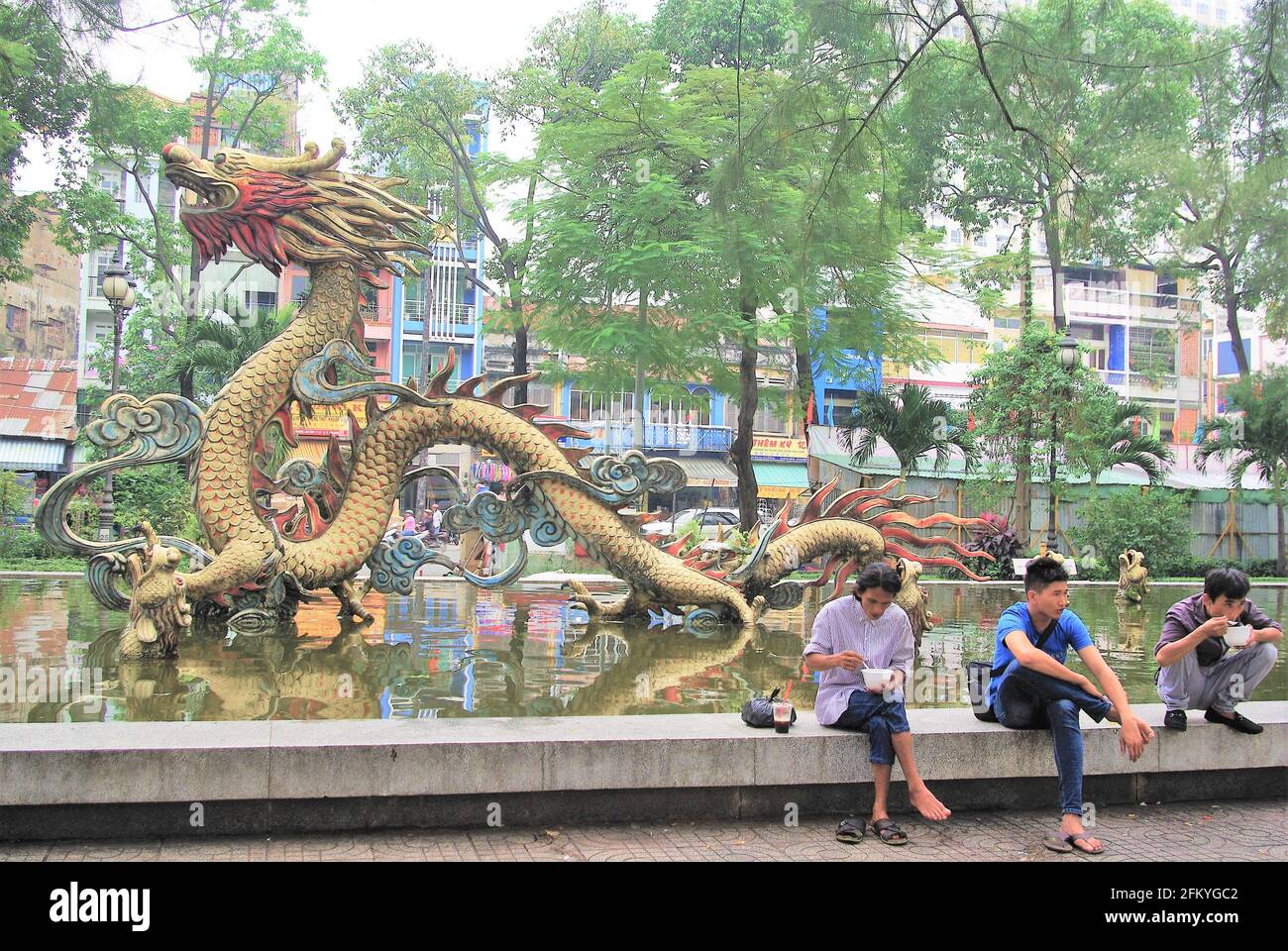 Street scene of 3 friends on lunchbreak at ornamental gardens with pond and dragon sculpture, Chinatown, Ho Chi Minh City, Vietnam, Asia Stock Photo