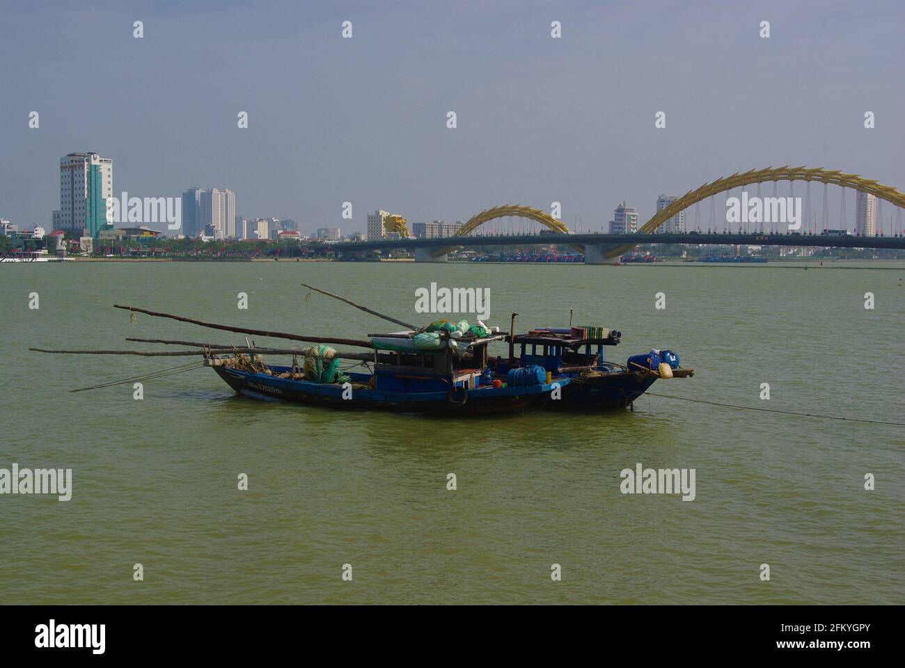 Working boats with Dragon Bridge on Han River, Da Nang, Vietnam, Asia Stock Photo