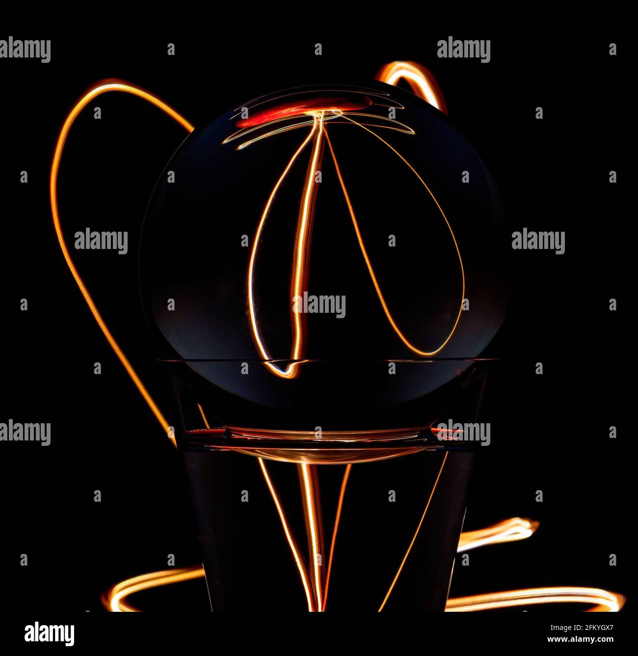 Light painting refraction caused by light traveling through a round glass globe atop a glass filled with water and reflecting its background.. Stock Photo