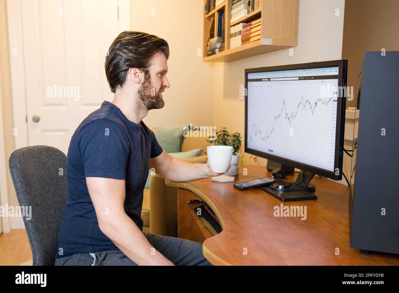 Man looking at finance chart on computer, day trader, investing from home, sipping coffee, relaxed man Stock Photo