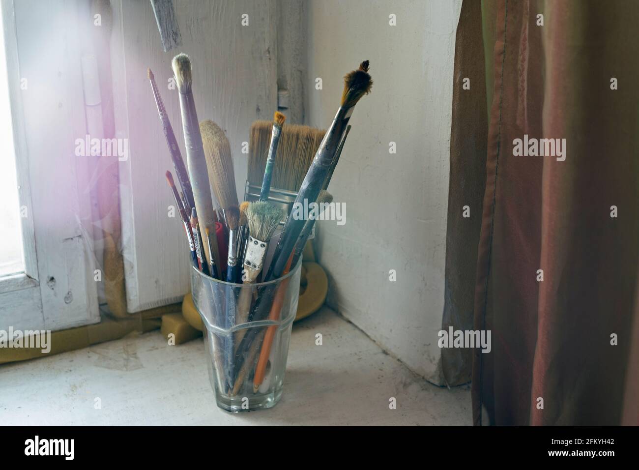 Painting brushes in the glass on the old windowsill. Selective focus on brushes. Blurred background Stock Photo