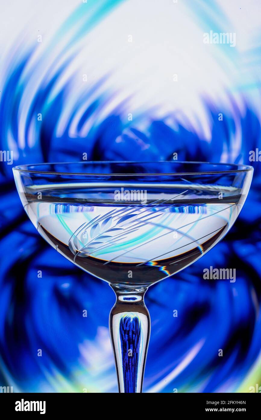 Refraction of a blue flower background closeup reflected in the etched crystal foreground glass Stock Photo