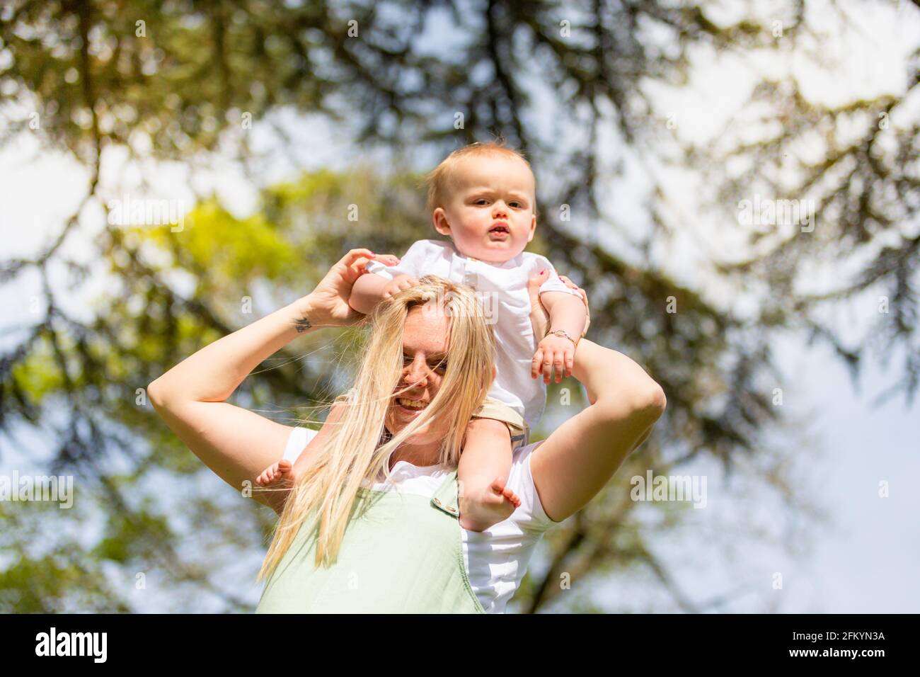 Young smiling mother with her baby son on her shoulders outdoors among nature Stock Photo