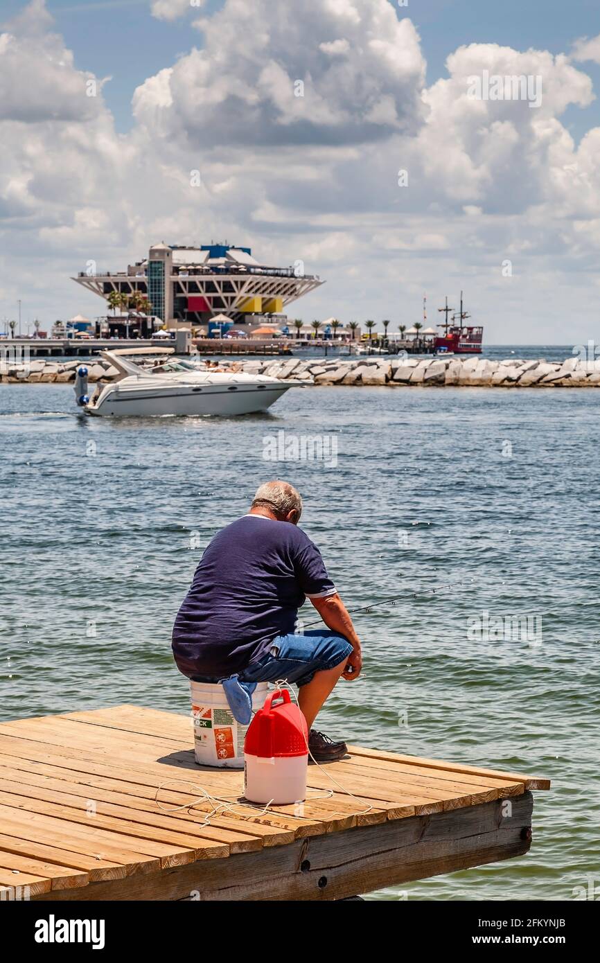Elderly man fishing from pier in St. Petersburg, Florida with yacht and St. Petersburg Pier in background. Building shown is the five-story inverted p Stock Photo