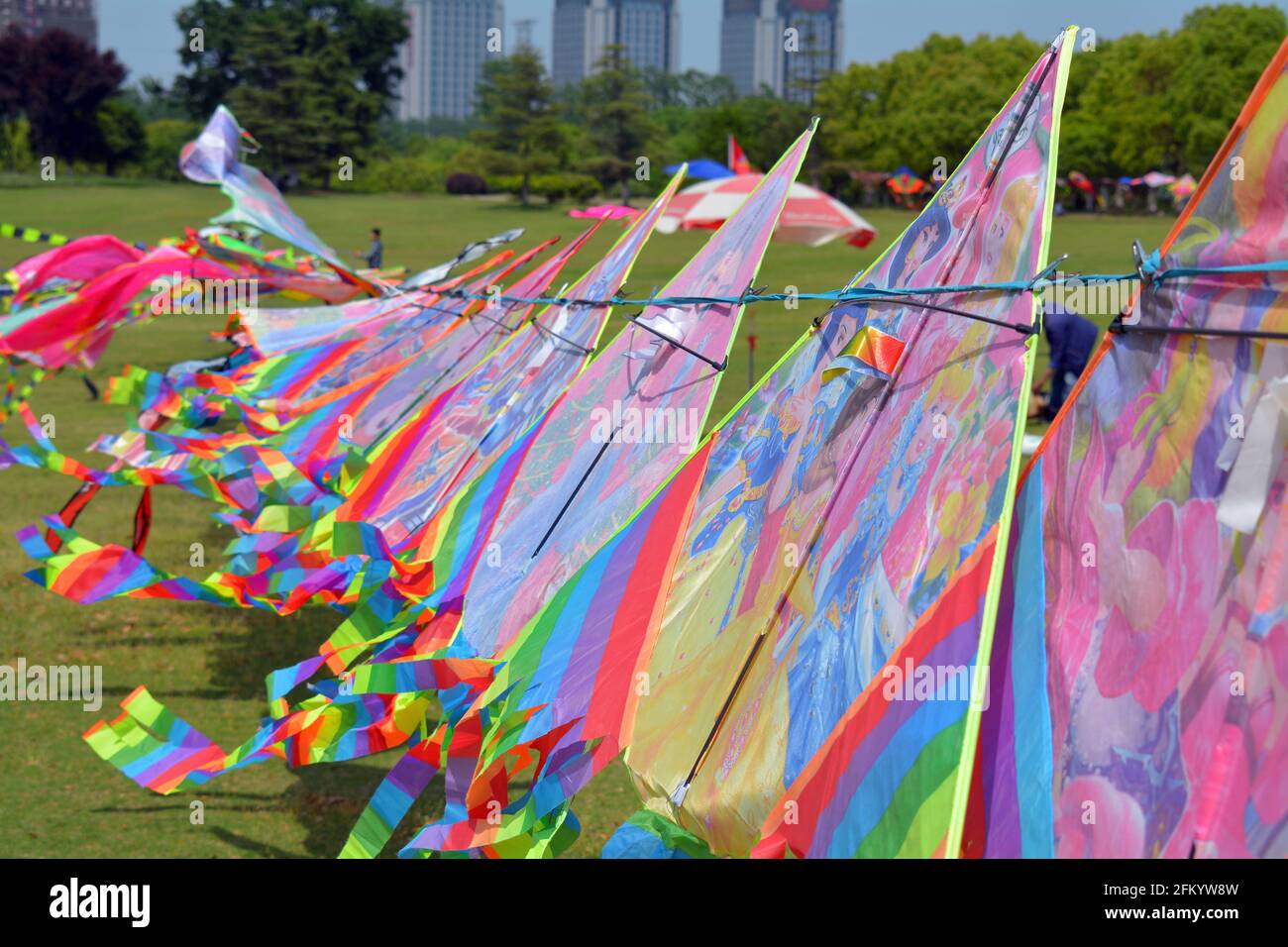 Line of bright rainbow coloured kites for sale in a park, flapping in