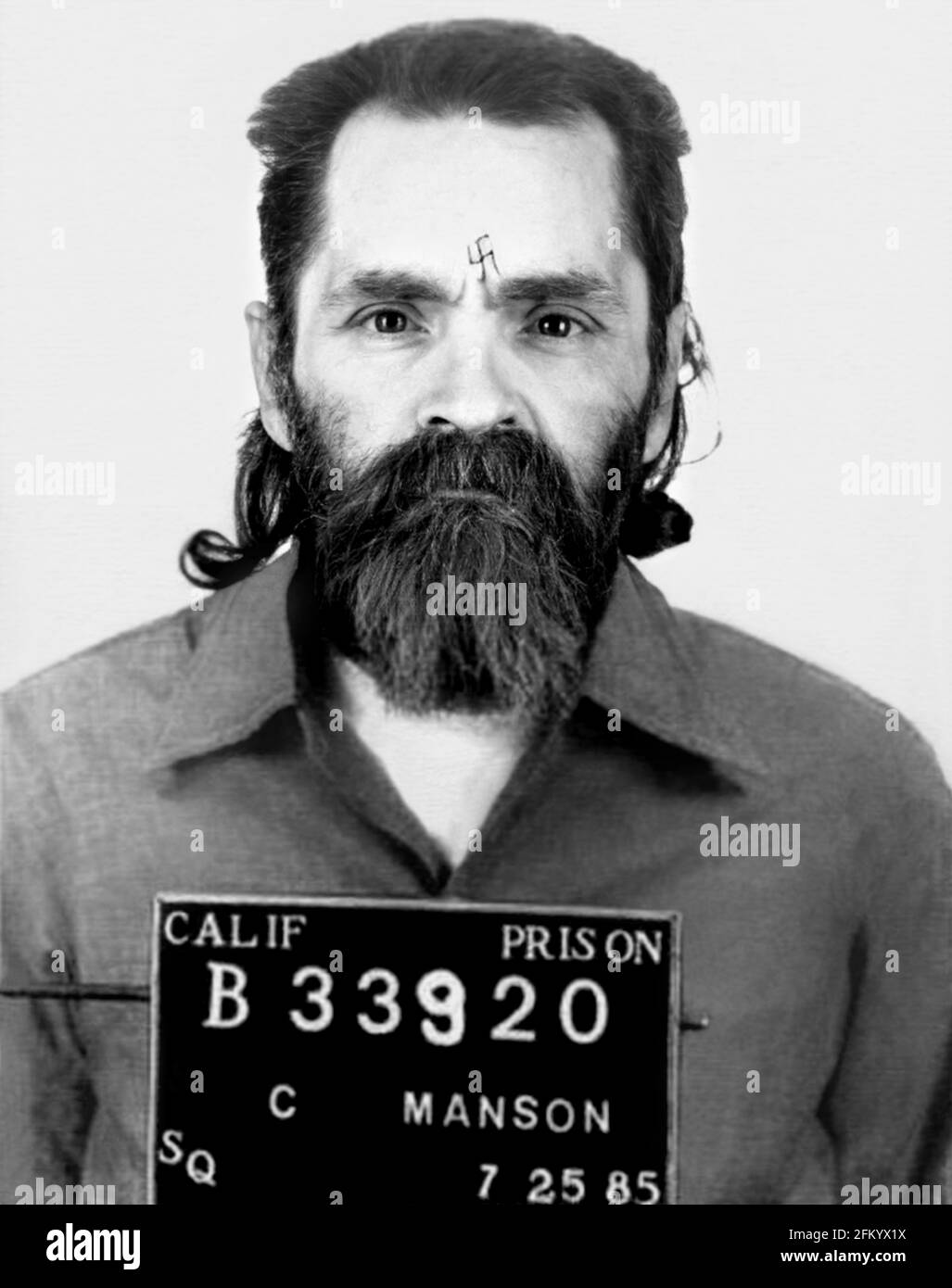 1985 , 25 july , USA : Mugshot of famous american satanist cult leader and criminal killer CHARLES MANSON SATANA ( 1934 - 2017 ). In mid-1967, he formed what became known as the ' Manson Family ', a quasi-commune based in California. His followers committed a series of nine murders at four locations in July and August 1969 . In 1971, he was convicted of first-degree murder and conspiracy to commit murder for the deaths of seven people, including the film actress Sharon Tate . Unknown photographer of California Prison . - MUGSHOT - Mug Shot - Mug-Shot - SVASTICA nazista - nazi nazist SVASTIKA - Stock Photo