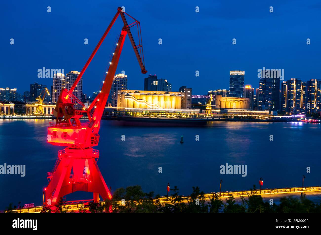 An old shipping crane in Yanpu District frames a cargo boat and buildings on the Pudong side of the Huangpu River, Shanghai, China. Stock Photo