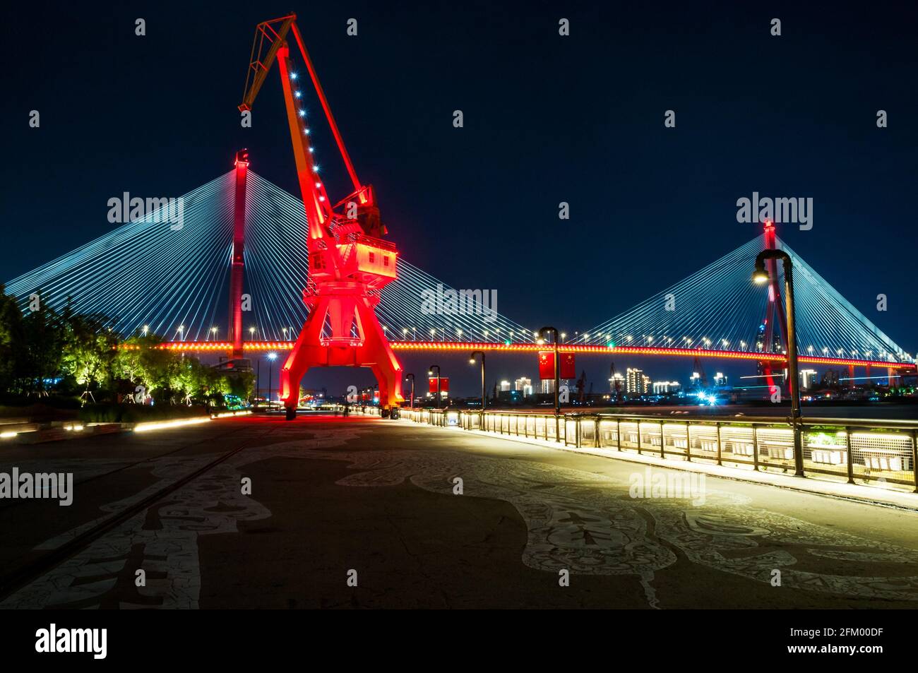 An old shipping crane on the Huangpu River waterfront at night with the Yangpu Bridge behind in Yangpu District, Shanghai, China. Stock Photo
