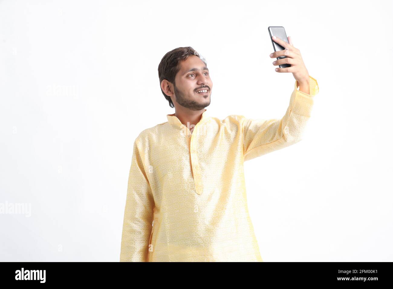 Indian man in traditional wear and taking selfie in smartphone Stock