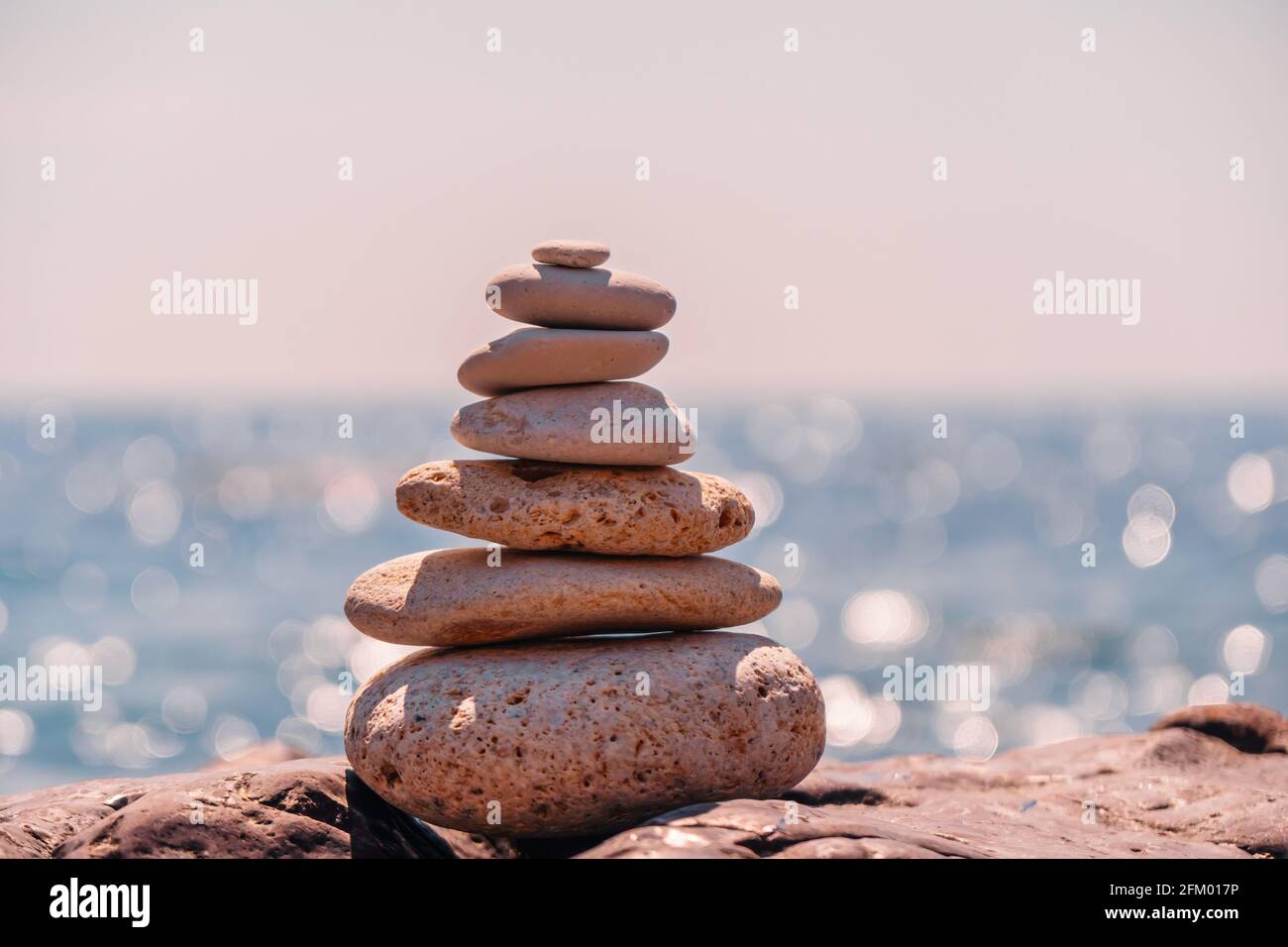 Pyramid stones on the seashore on a sunny day on the blue sea background. Happy holidays. Pebble beach, calm sea, travel destination. Concept of happy Stock Photo