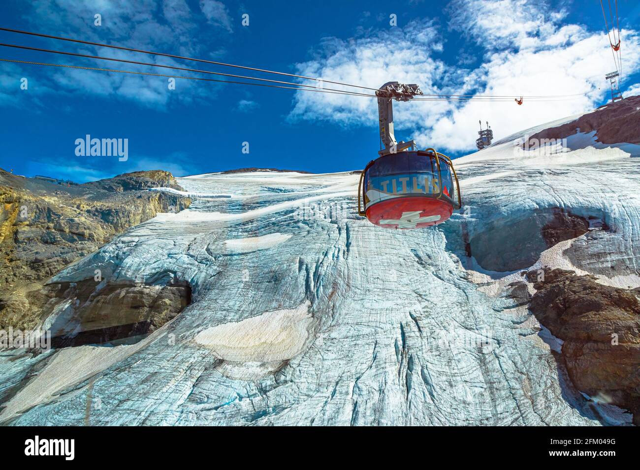 Titlis, Engelberg, Switzerland - Aug 27, 2020: cable car with Swiss flag moving to Titlis icy peak of snowy Uri alps. Located in cantons of Obwalden Stock Photo