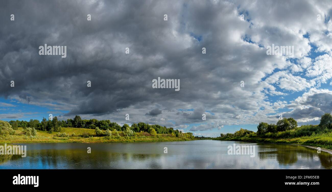 Stormy dramatic sky over the calm lake and green hills during sunset.Beautiful panoramic landscape. Stock Photo