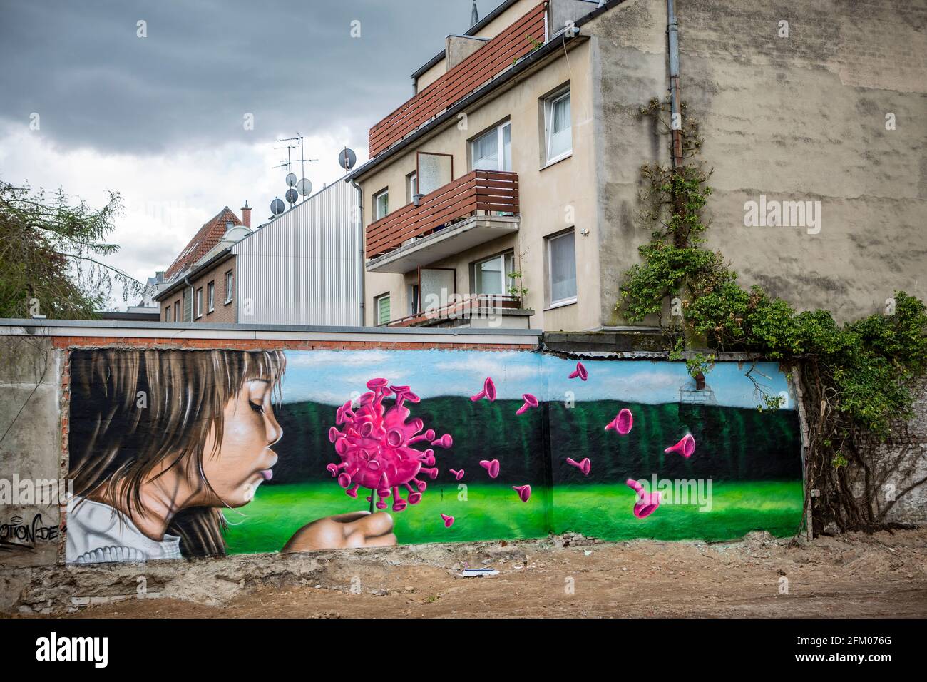 Ein Graffiti an einer alten Mauer zeigt ein Mädchen, welches wie bei einer Pusteblume ein Coronavirus anpustet, welches dann auseinander fliegt. Ein s Stock Photo