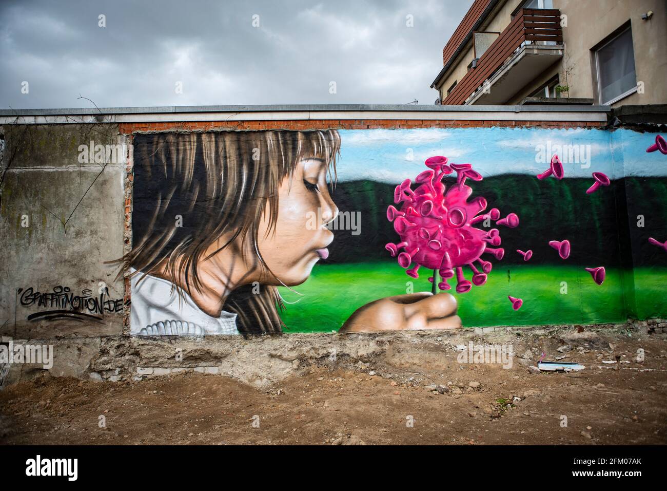 Ein Graffiti an einer alten Mauer zeigt ein Mädchen, welches wie bei einer Pusteblume ein Coronavirus anpustet, welches dann auseinander fliegt. Ein s Stock Photo