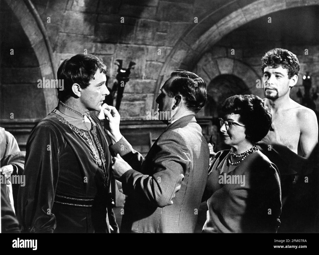 RICHARD BURTON has his make-up touched up while PETER O'TOOLE looks on candid on set during filming of BECKET 1964 director PETER GLENVILLE play Jean Anouilh and Lucienne Hill screenplay Edward Anhalt costume design Margaret Furse producer Hal B. Wallis  Wallis-Hazen A Paramount Film Service & Keep Films Co-Production / Paramount Pictures Stock Photo