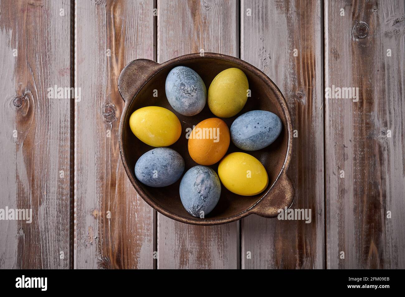 Homemade Easter multi-colored painted eggs on ceramic platter against a background of textured boards. Top view, copy space Stock Photo