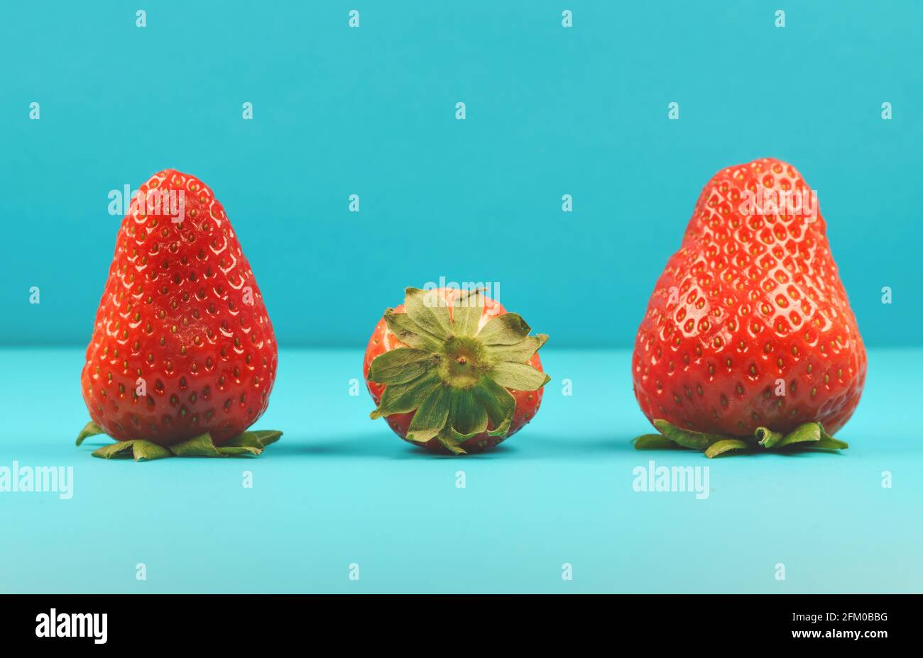 Detail of three fresh red strawberries on turquoise background as a symbol for summer and happiness Stock Photo