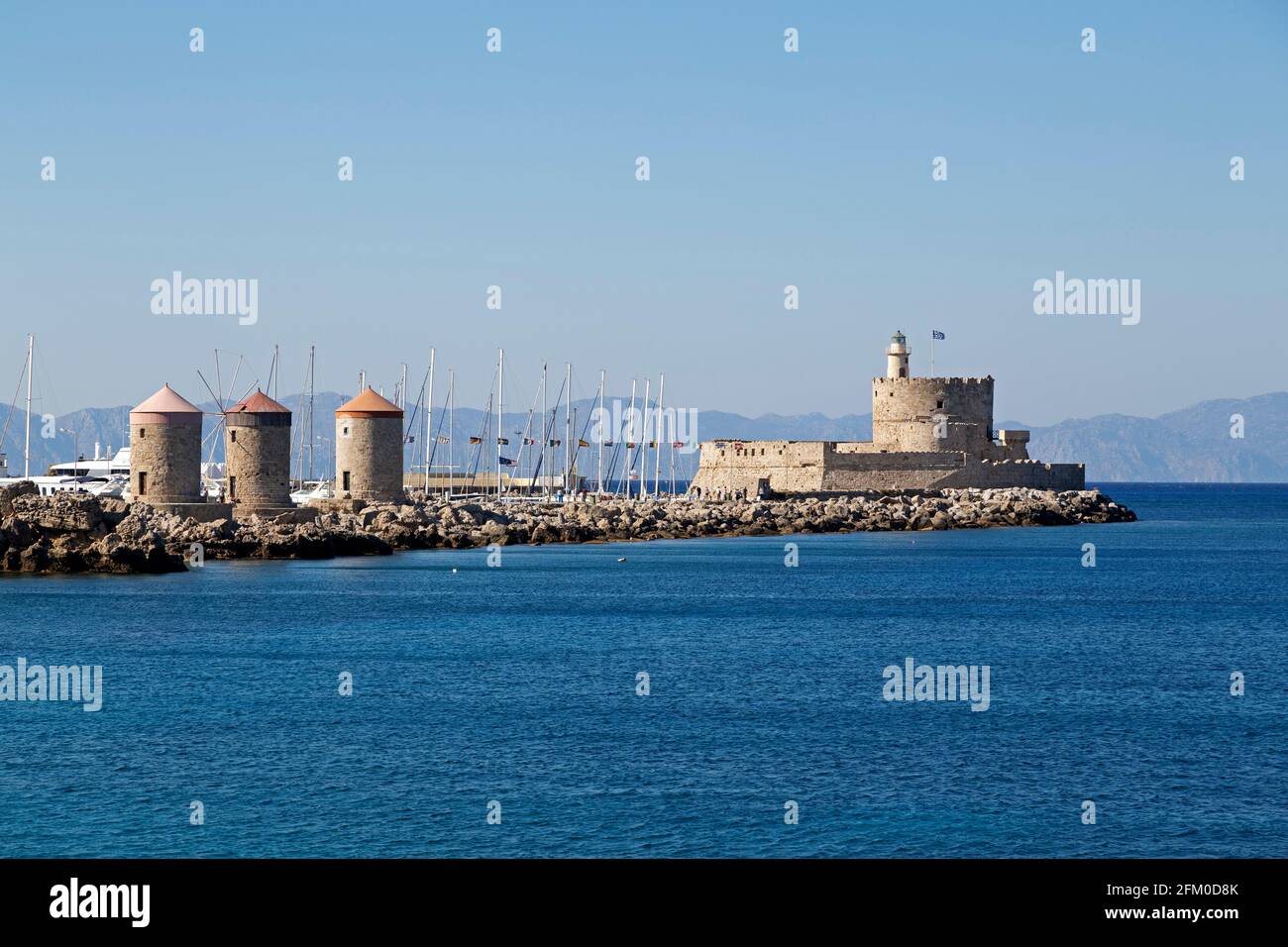 The Fort of St Nicholas in the city of Rhodes in Greece. The 15th century fortress iis on a harbour wall with the three stone Windmills of Mandraki. Stock Photo
