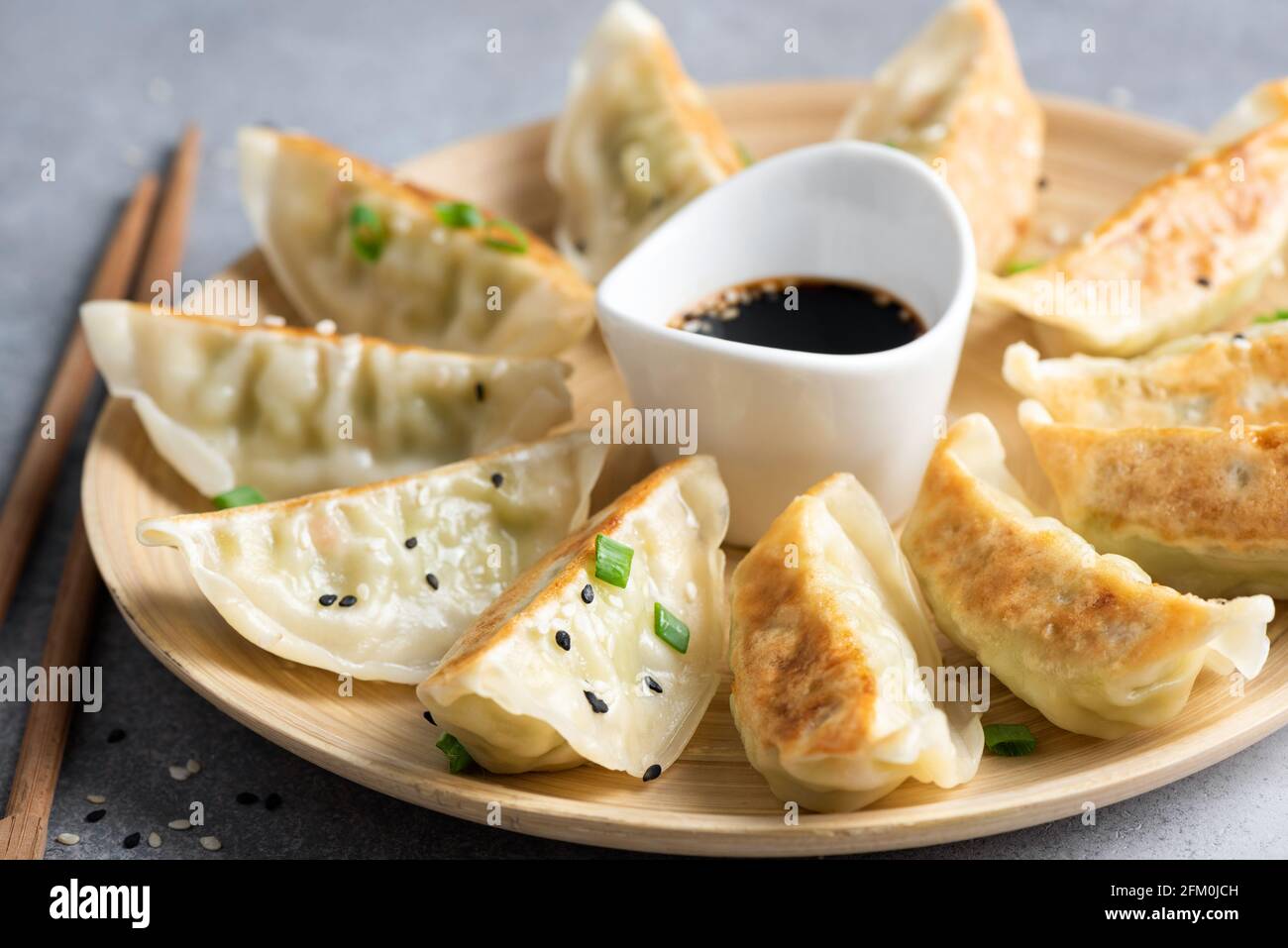 Gyoza or jiaozi fried stuffed dumplings on a bamboo plate, closeup view Stock Photo