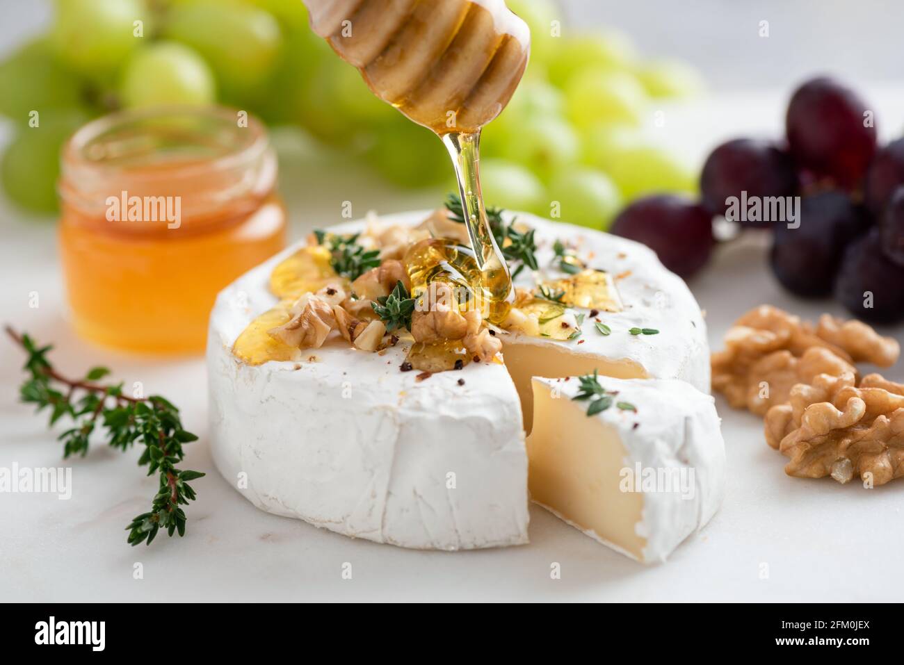 Honey pouring on camembert cheese with walnuts and grapes. Gourmet