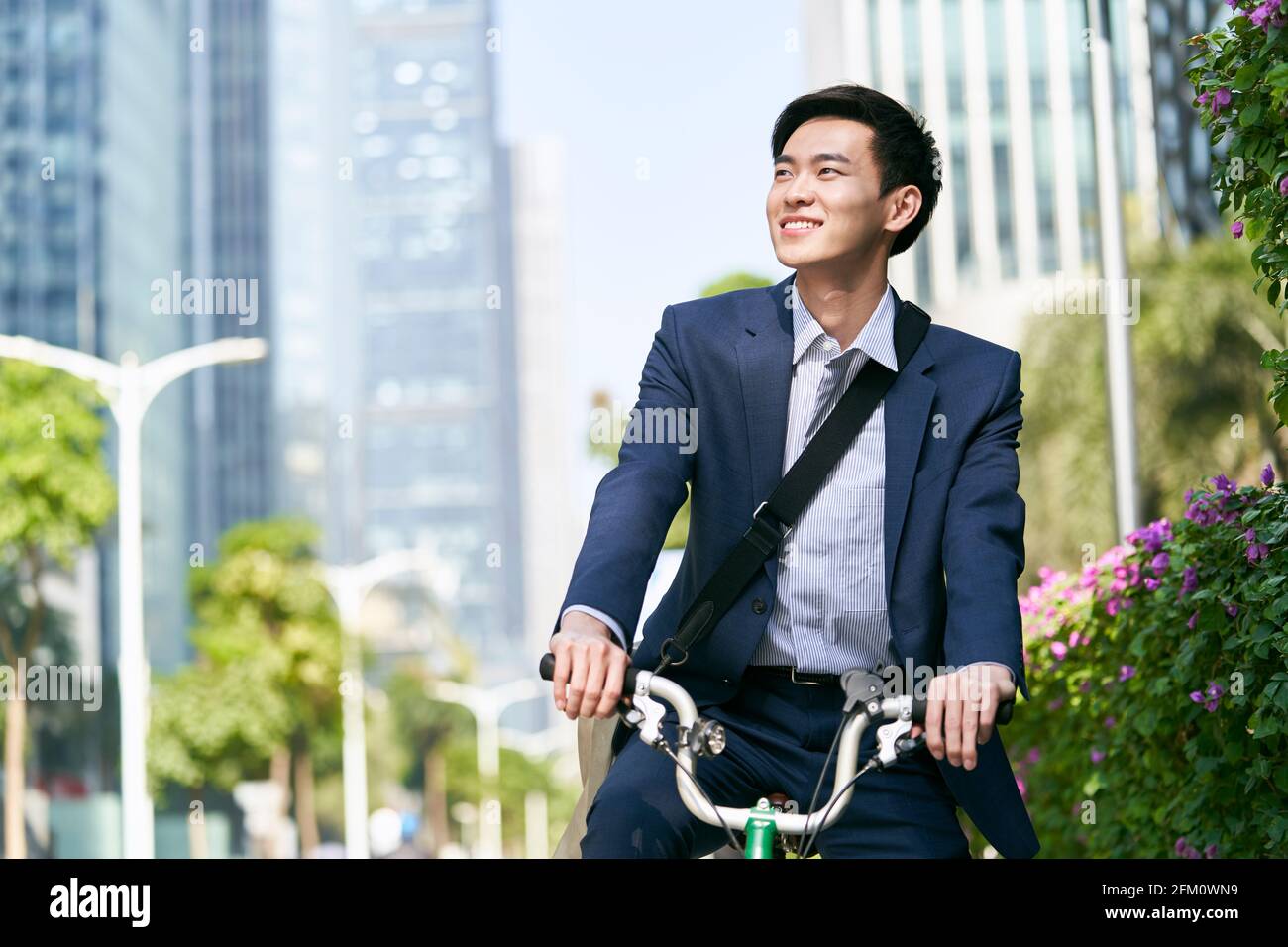 young asian business man riding bicycle in downtown financial district of modern city, happy and smiling Stock Photo