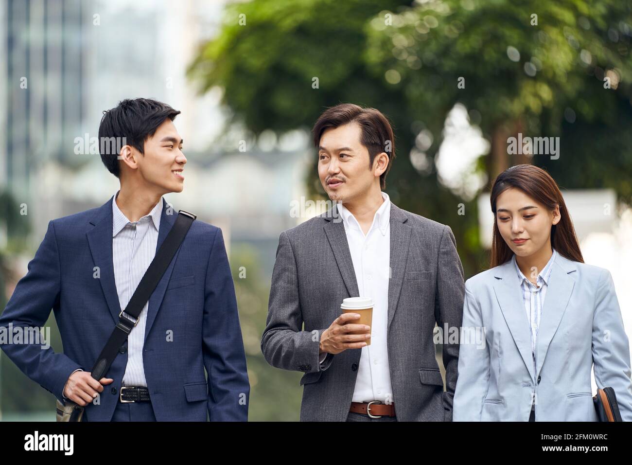 three asian business people walking talking on street Stock Photo