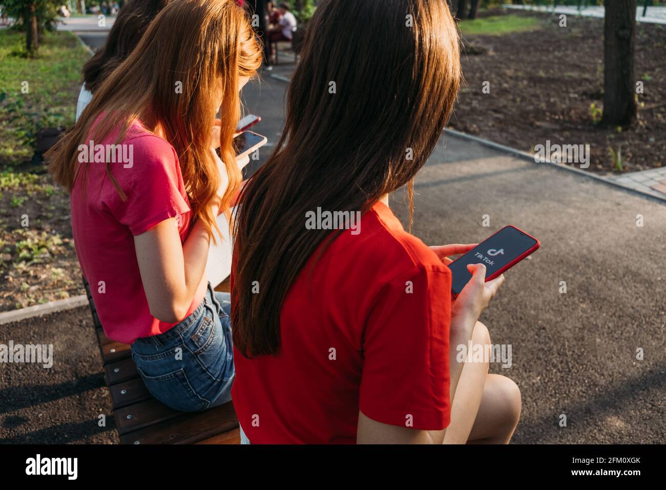 Three girls chatting with their smartphones at the park. Gen Z young girl friends using gadget and having fun outdoors. Kropivnitskiy, Ukraine, June Stock Photo