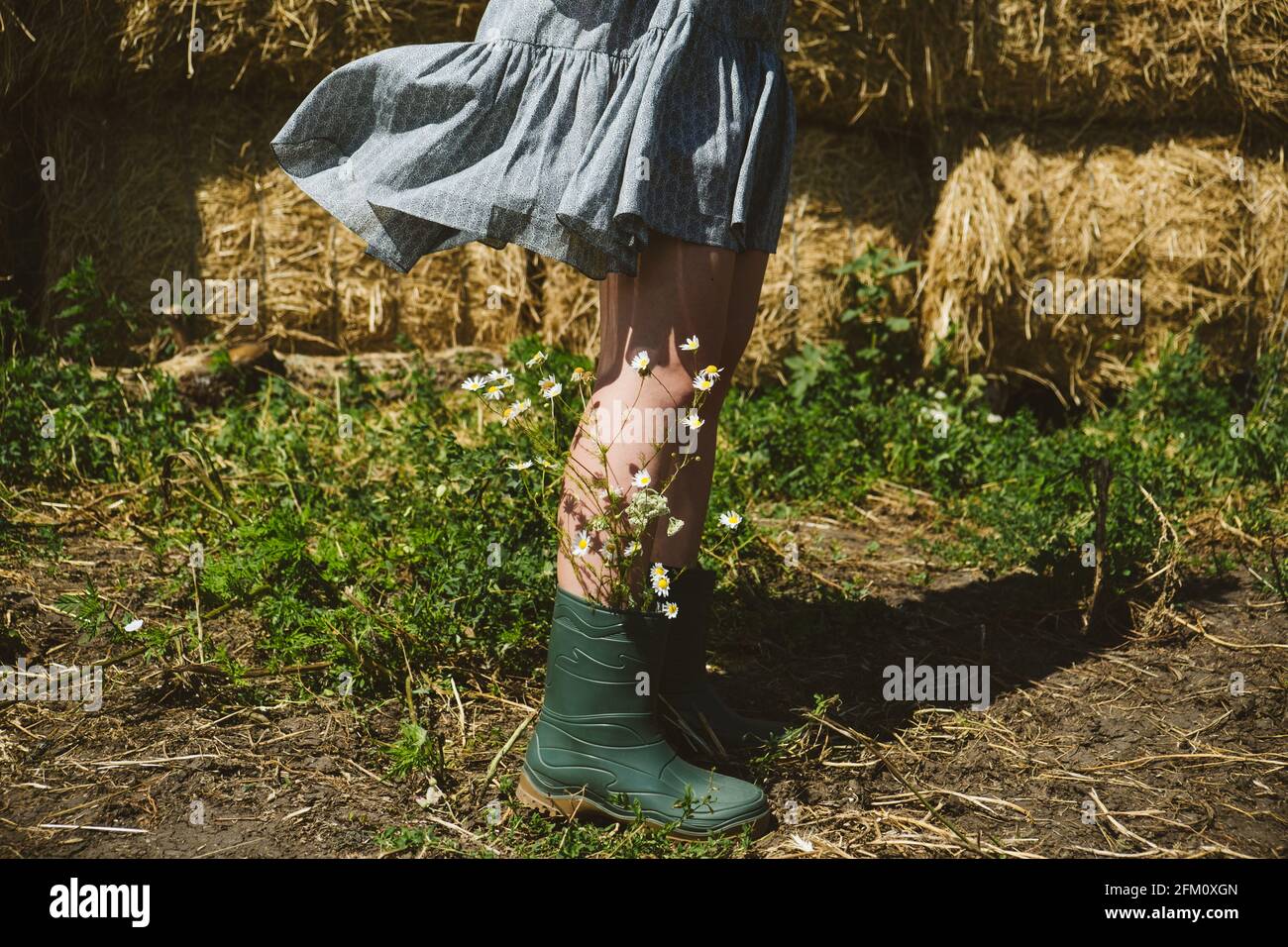 Young girl in rubber boots with flowers standing against the background ...