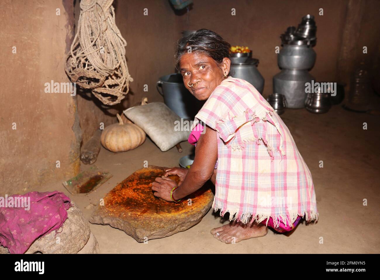 Tribal old woman using a traditional stone grinder to grind red chilly at Boriborivalsa Village, Araku, Andhra Pradesh, India. PARANGIPERJA TRIBE Stock Photo