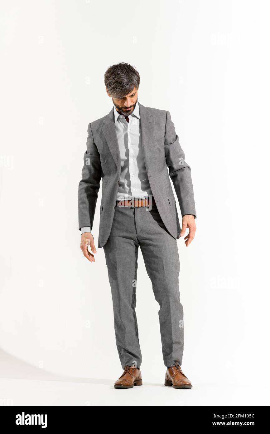 Handsome man in smart suit stood looking downwards on a white background Stock Photo