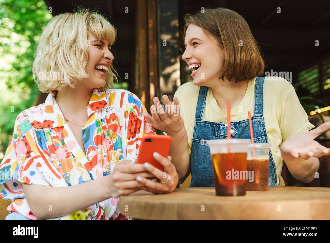 Image of happy caucasian two women using cellphones and laughing while ...