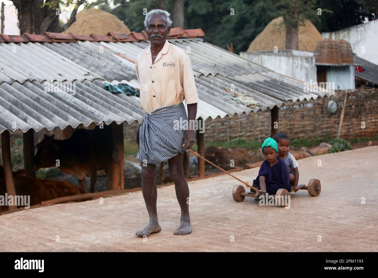 Bhakta tribal old man pulling small kids in a wooden toy cart at Hattaguda village, Andhra Pradesh, India Stock Photo