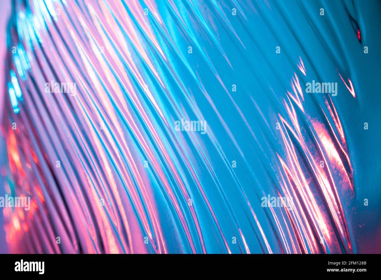 Abstract glass background. Texture of wavy glass illuminated with multi-colored light. Pink and blue stains. Close up. Flares on glass Stock Photo