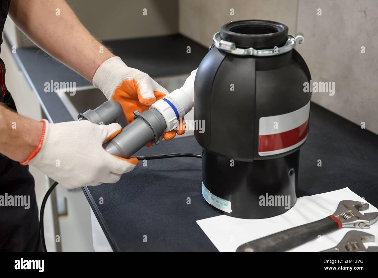 A worker is installing a household waste shredder for the kitchen sink