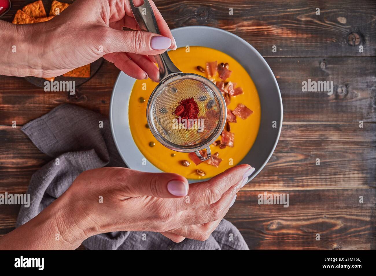 Woman's hands sprinkled with sieve paprika on traditional pumpkin puree cream soup with carrots, onions, ginger, garlic, coconut milk. Healthy, vegetarian food. Top view, selective focus Stock Photo