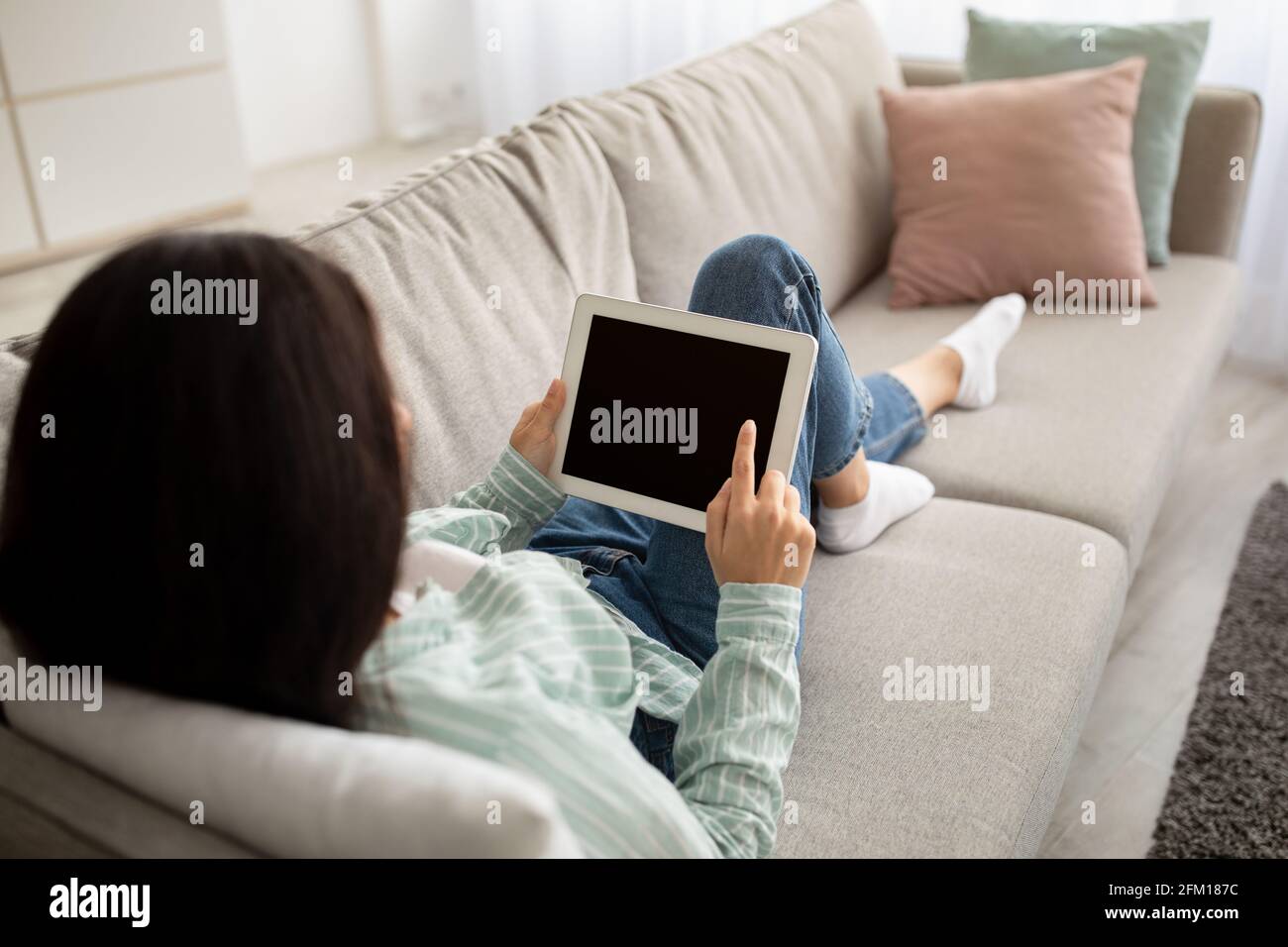 Unrecognizable indian woman with tablet pc sitting on comfy sofa and