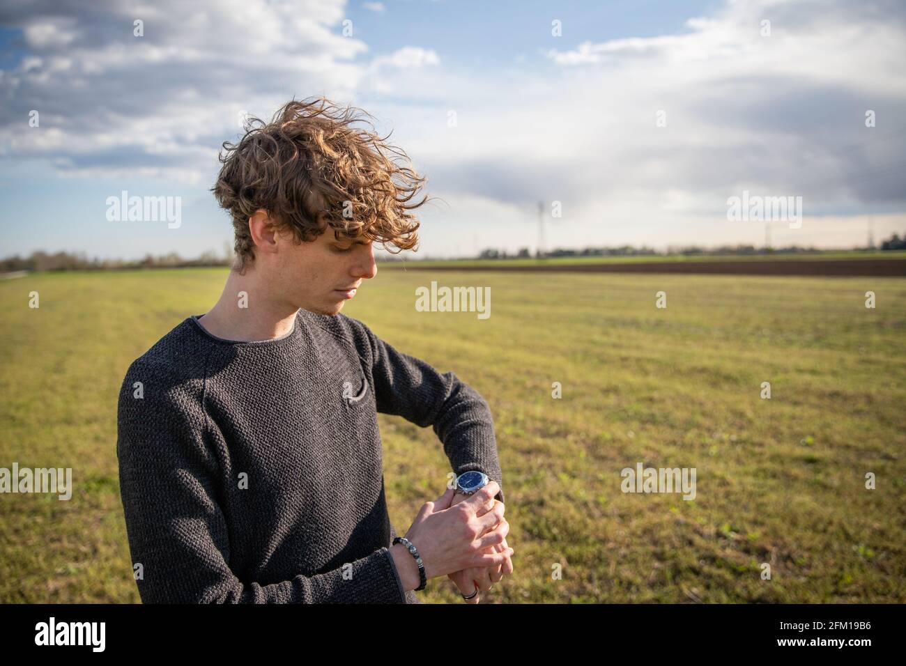Attractive caucasian boy watches the time on his watch in a meadow Stock Photo