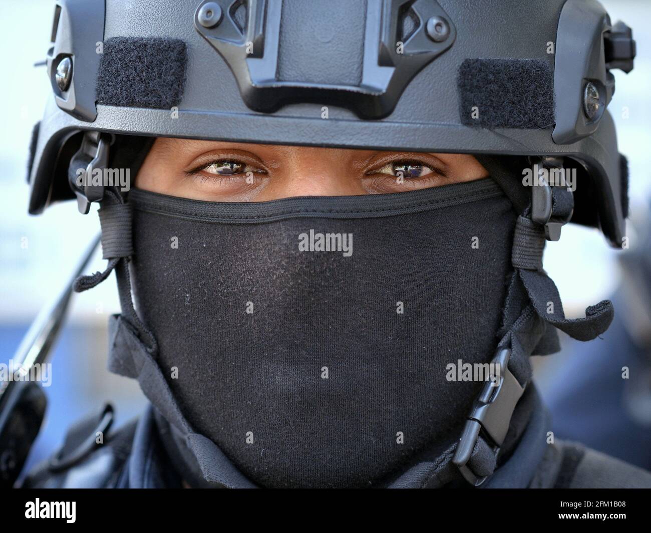 Young Caucasian tactical motorcycle police officer wears black personal protective equipment with helmet and black face mask and looks at the viewer. Stock Photo