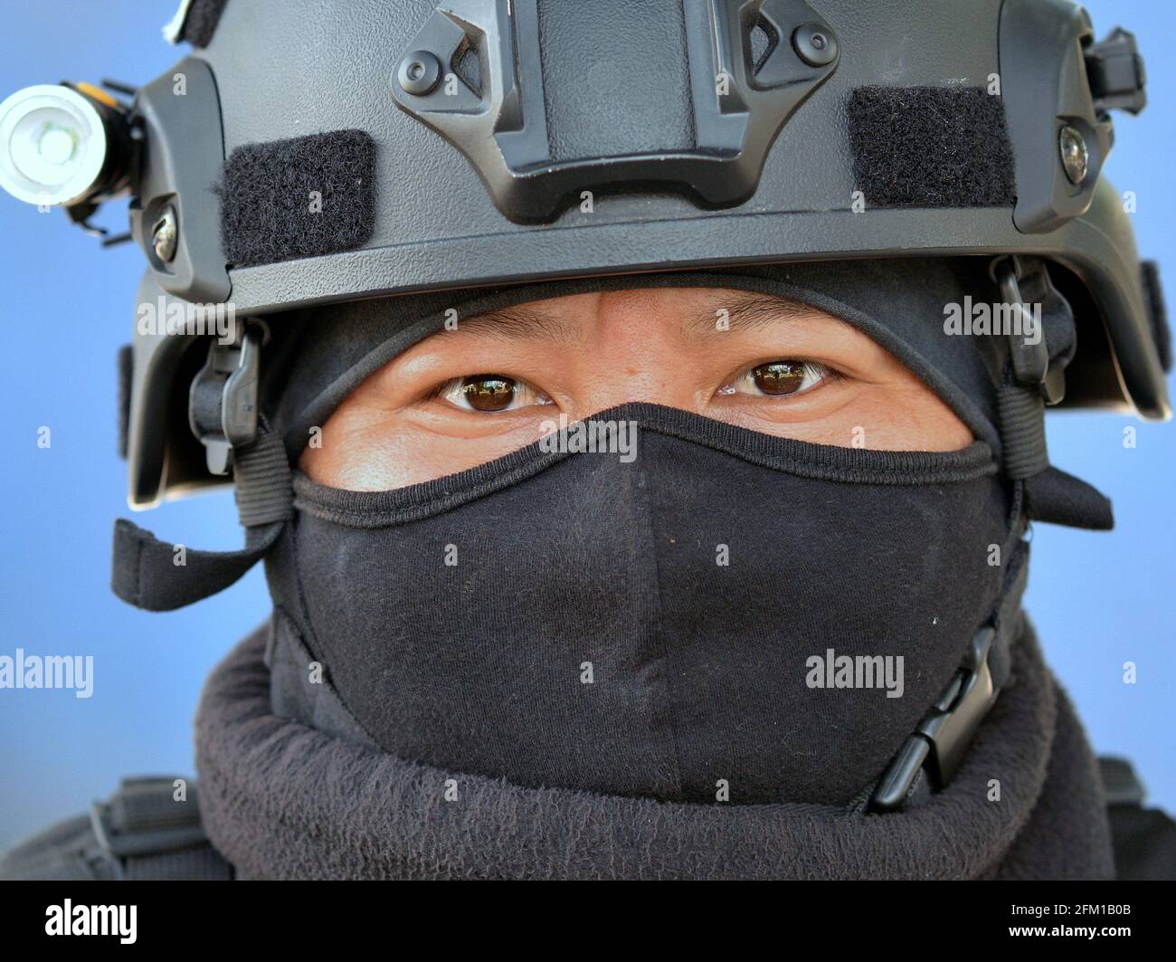 Young tough tactical motorcycle police officer wears personal protective equipment and a black balaclava and looks with weary eyes at the viewer. Stock Photo
