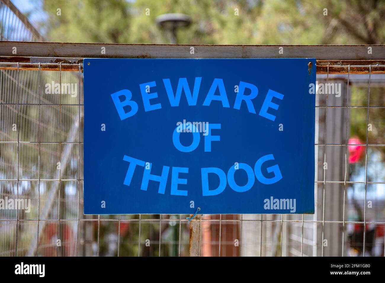 Beware of the dog, Warning messagel, text on blue sign. Label on metal rusty wire mesh fence background inform about caution, danger canine attack, at Stock Photo