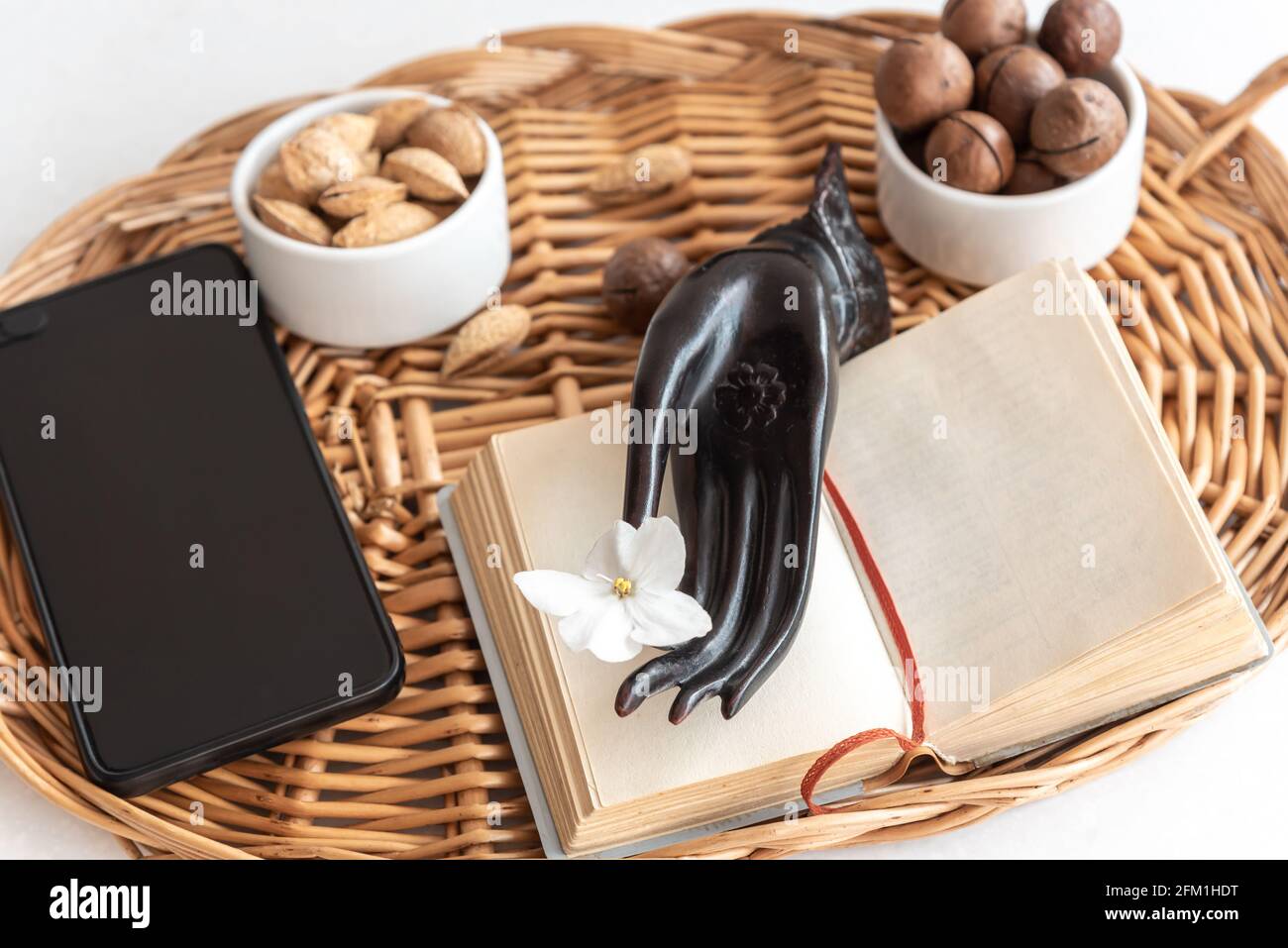 A open book or notebook, smartphone and a snack of nuts on a table in a wicker tray. Stock Photo