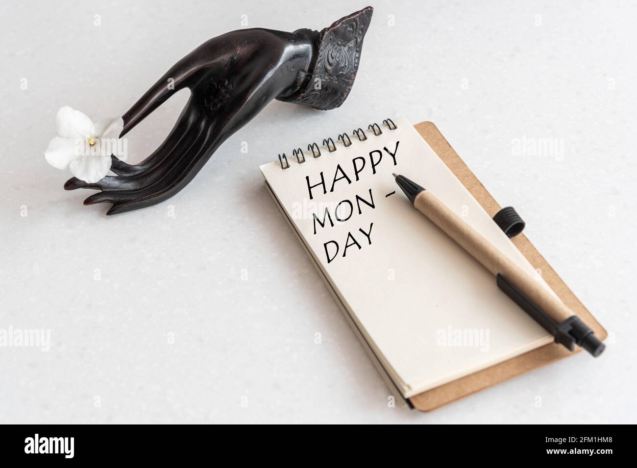 Happy Monday Word in open notebook and flower in black hand. White Office Workplace Stock Photo