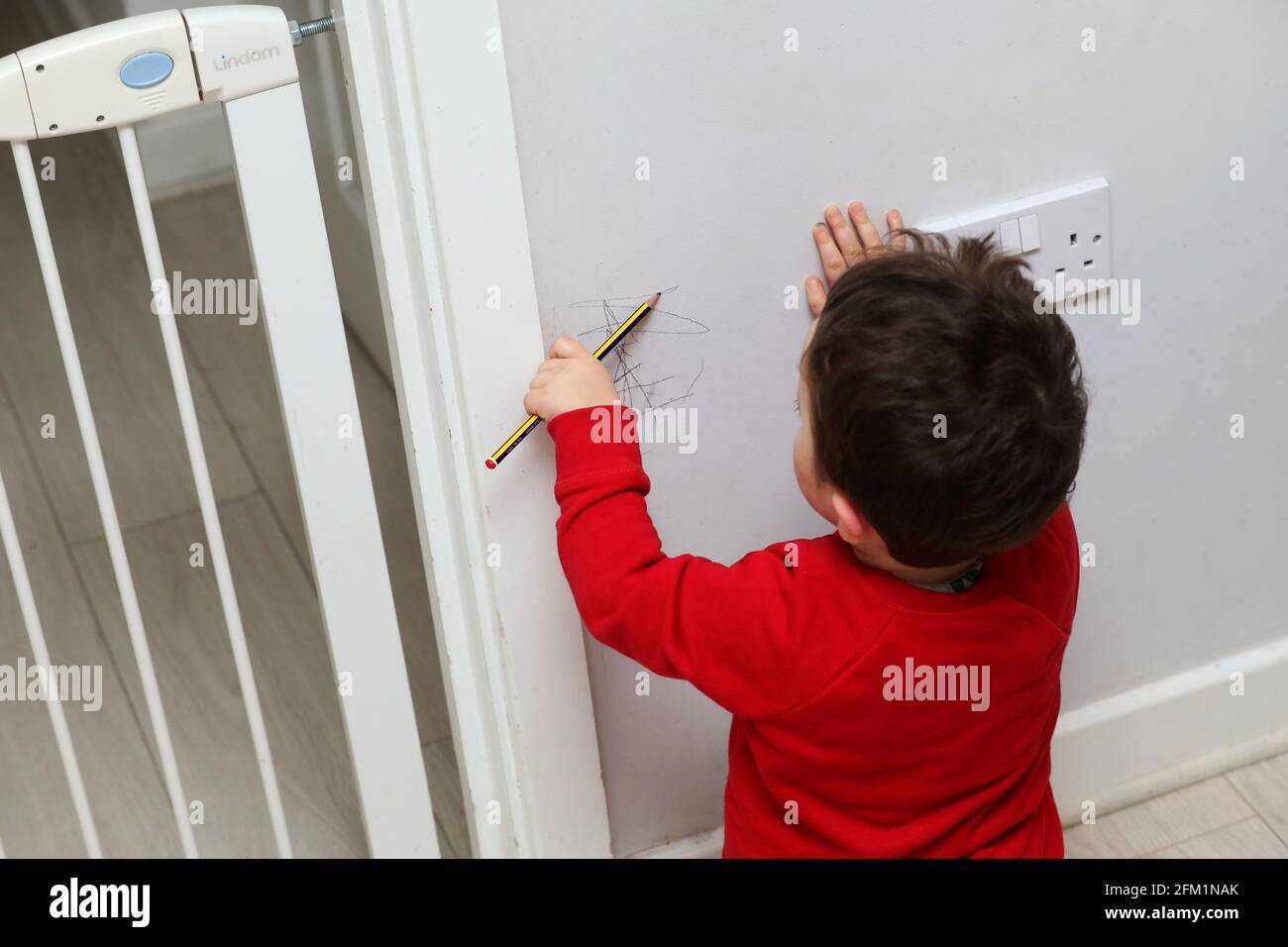 A young boy pictured drawing on the walls with a pencil in West Sussex, UK. Stock Photo